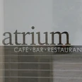 Atrium Schriftzug "Atrium Café Bar Restaurant" auf einer Glasoberfläche, dahinter verschwommene Gebäudestrukturen.