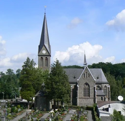 Kirche St. Margareta Kirche im gotischen Stil mit hohem Turm und Spitzdach, umgeben von Friedhof und grüner Landschaft.