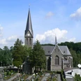 Kirche St. Margareta Kirche im gotischen Stil mit hohem Turm und Spitzdach, umgeben von Friedhof und grüner Landschaft.