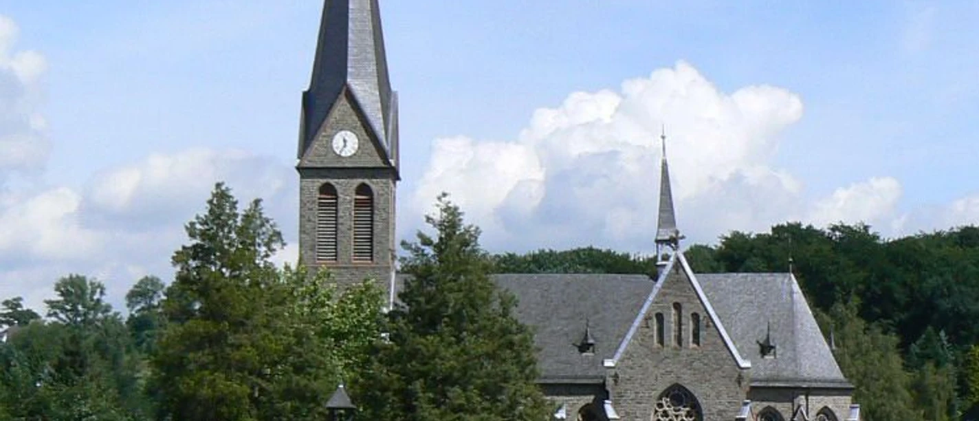 Kirche St. Margareta Kirche im gotischen Stil mit hohem Turm und Spitzdach, umgeben von Friedhof und grüner Landschaft.