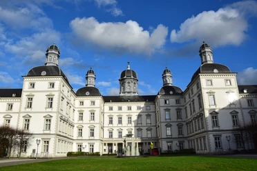 Schloss Bensberg Barockes Schloss mit symmetrischer Fassade, vier Türmen und blauem Himmel, umgeben von Rasenfläche.