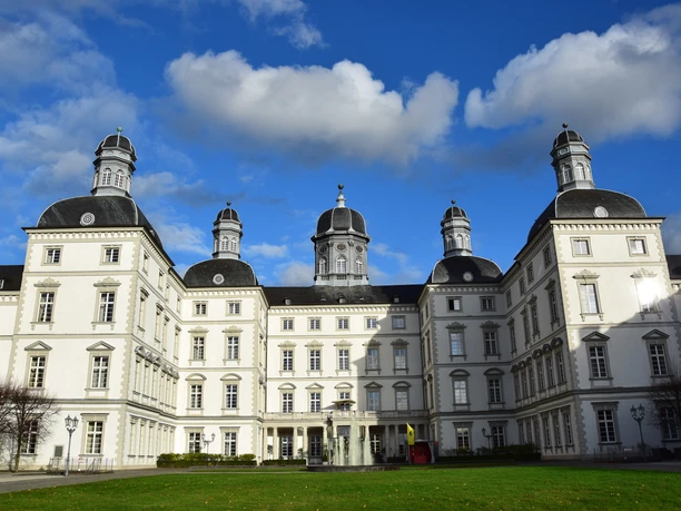 Schloss Bensberg Barockes Schloss mit symmetrischer Fassade, vier Türmen und blauem Himmel, umgeben von Rasenfläche.
