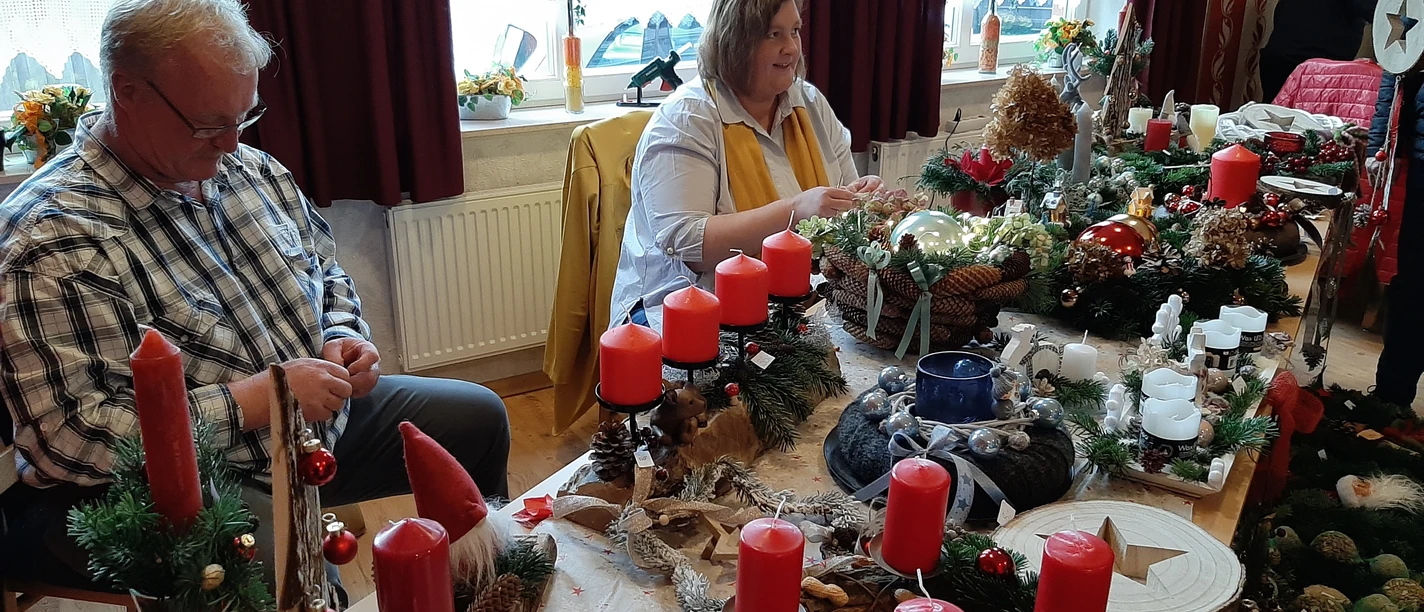People selling Advent arrangements with red candles and fir branches on a Christmas table.