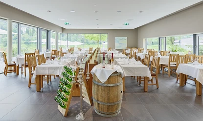 Hotel Elbresidenz Restaurant Elbterrasse Helles Restaurant mit Holzmöbeln, weiß gedeckten Tischen, Weinfass und Flaschenregal; große Fenster bieten Blick ins Grüne.
