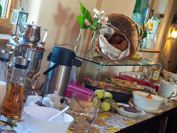Menschen sitzen an Holztischen unter gelben und grünen Sonnenschirmen in einem Biergarten mit Holzhütte, umgeben von Pflanzen.People sit at wooden tables under yellow and green parasols in a beer garden with a wooden hut, surrounded by plants.Lidé sedí u dřevěných stolů pod žlutými a zelenými slunečníky v pivní zahrádce s dřevěnou chatkou, obklopené rostlinami.Ludzie siedzą przy drewnianych stołach pod żółtymi i zielonymi parasolami w ogródku piwnym z drewnianą chatą, otoczoną roślinami.Mensen zitten aan houten tafels onder gele en groene parasols in een biertuin met een houten hut, omringd door planten.Le persone siedono a tavoli di legno sotto ombrelloni gialli e verdi in una birreria all'aperto con una capanna di legno, circondata da piante.
