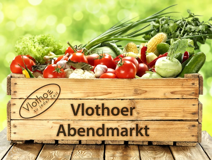 Vlothoer Abendmarkt Eine Holzkiste voller bunter, frischer Gemüsearten wie Tomaten, Paprika und Mais vor grünem Hintergrund.