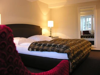 Doktorplatz.jpg Doppelzimmer mit stilvollem Design, weicher Tagesdecke, Nachttischlampe und gemütlicher Beleuchtung.