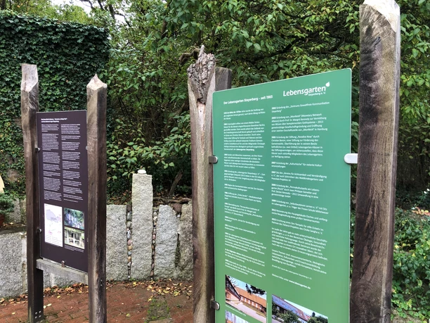 Lebensgarten Steyerberg with information boards surrounded by lush greenery and natural stones.
