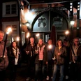 Fackel.jpg Menschen halten Fackeln vor einem beleuchteten, historischen Fachwerkgebäude in abendlicher Szenerie.
