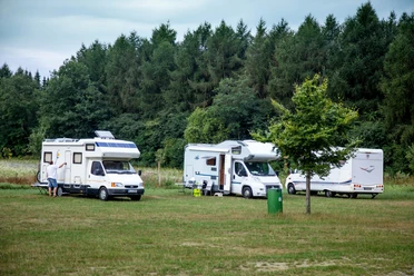 Wohnmobile Lopausee Drei weiße Wohnmobile parken auf einer grünen Wiese vor einem Wald am Lopausee.