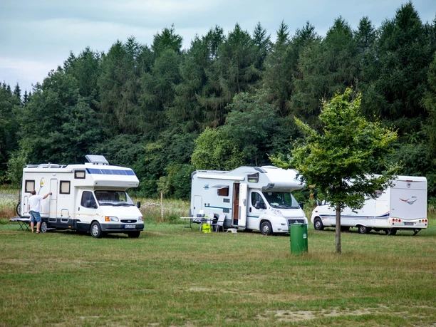 Wohnmobile Lopausee Drei weiße Wohnmobile parken auf einer grünen Wiese vor einem Wald am Lopausee.