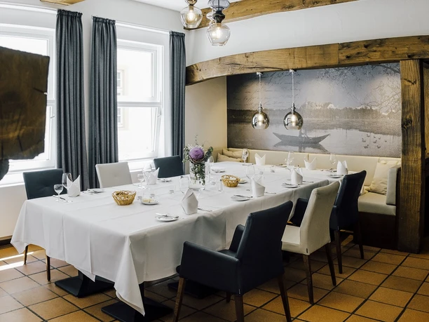 Ein eleganter, gemütlicher Speiseraum mit gedecktem Tisch, rustikalen Holzbalken und einer idyllischen Wandmalerei.