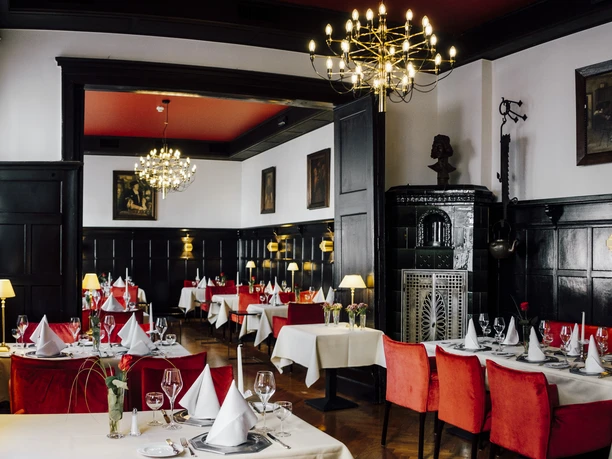 Elegantes Restaurant mit roten Polstern, weißen Tischdecken und Kronleuchtern in stilvollem Ambiente.