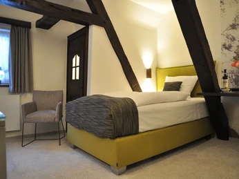 Gemütliches Schlafzimmer mit modernem Design, Einzelbett, Holzbalken und natürlichem Licht.