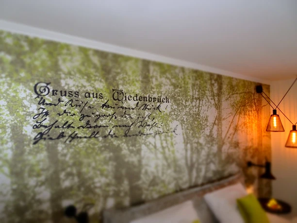 Wandgestaltung mit Waldmotiv und nostalgischem Schriftzug "Gruss aus Wiedenbrück" in beleuchtetem Raum.