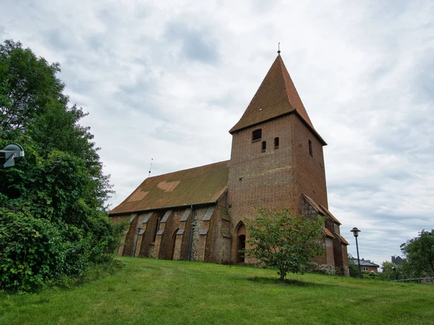 St. Martins-Kirche in Soderstorf Die historische St. Martins-Kirche aus Backstein mit spitzem Turmdach steht auf einem grünen Hügel.