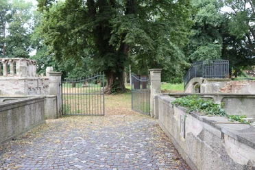 Ellerburg Historisches Tor mit schmiedeeisernen Flügeltüren führt in eine von Bäumen gesäumte, ruhige Gartenanlage.