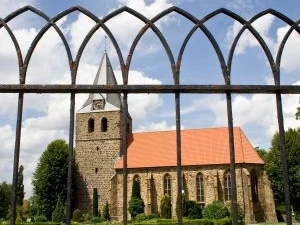 Gehlenbeck-Kirche.jpg Eine historische Kirche aus Stein mit rotem Dach hinter einem schwarzen, schmiedeeisernen Gitter.