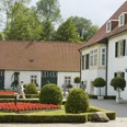 Historisches Gebäude mit gepflegtem Garten, roten Blumenbeeten und grünen Bäumen im Hintergrund.