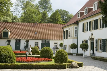 Pr-Oldendorf - Haus des Gastes Historisches Gebäude mit gepflegtem Garten, roten Blumenbeeten und grünen Bäumen im Hintergrund.