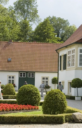 Pr-Oldendorf - Haus des Gastes Historisches Gebäude mit gepflegtem Garten, roten Blumenbeeten und grünen Bäumen im Hintergrund.