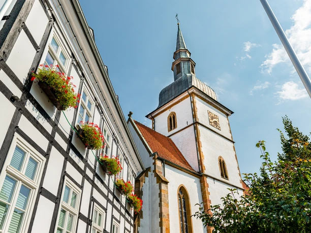 Rietberg-St-Joh-Baptist-K-prowiGT-Wallenfang.jpg Dreistöckiges Fachwerkgebäude mit Blumenkästen, daneben imposante weiße Kirche mit spitzem Turm.