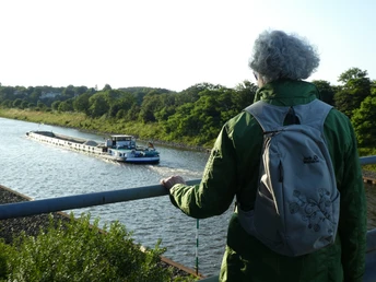 Schleusenkanal Etelsen Eine Person mit grünem Rucksack blickt auf ein Binnenschiff, das den Schleusenkanal Etelsen befährt.A person with a green rucksack looks at a barge navigating the Etelsen lock canal.En person med en grøn rygsæk kigger på en pram, der sejler gennem Etelsens slusekanal.Een persoon met een groene rugzak kijkt naar een binnenschip dat door het kanaal van de Etelsen sluis vaart.
