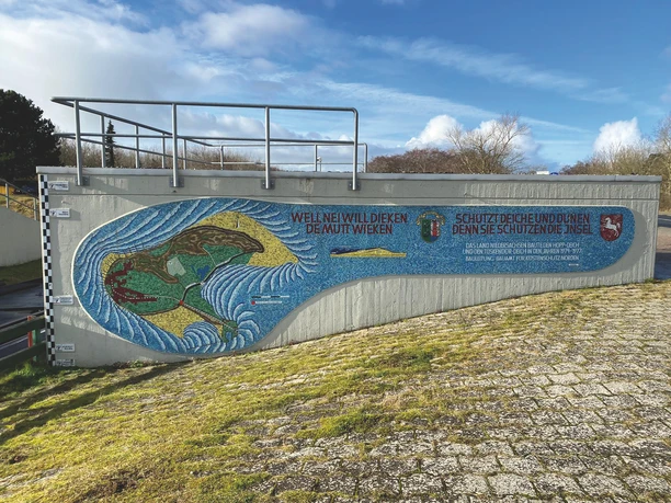 Mosaik Kunstwerk Informationstafel mit Borkum Umriss. An einer Steinmauer.