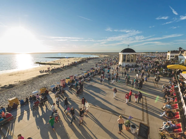 Promenade Die Promenade an der Nordsee zeigt bei Sonnenuntergang eine belebte, breite Gehzone mit Blick aufs Meer.