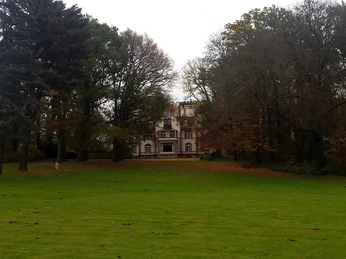 Park des Ritterguts Haus Morp mit Blick auf Villa Grillo (Forsthaus Morp) Eine Villa mit beeindruckender Fassade ragt hinter einem grünen Rasen, umgeben von Bäumen, empor.