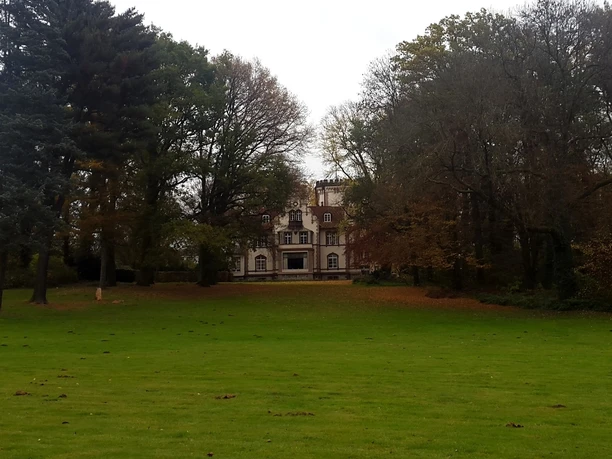 Park des Ritterguts Haus Morp mit Blick auf Villa Grillo (Forsthaus Morp) Eine Villa mit beeindruckender Fassade ragt hinter einem grünen Rasen, umgeben von Bäumen, empor.