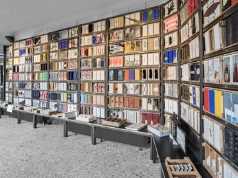 Grundsteinkiste in Velbert-Langenberg Vielzahl von Büchern in farbenfrohen Umschlägen geordnet in einem Regal auf grauem Boden.