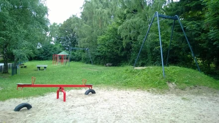 Kinderspielplatz an der Osterholzer Straße Spielplatz mit roter Wippe und Rutsche, umgeben von üppigem Grün und schattenspendenden Bäumen.