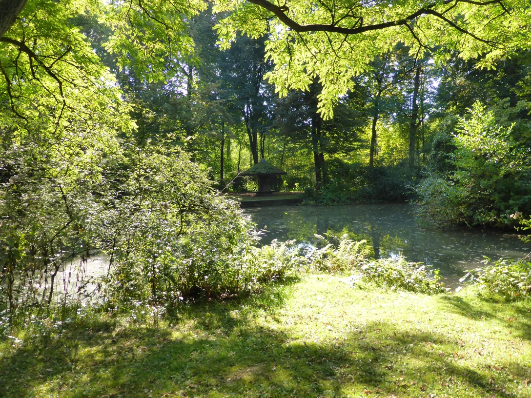 Teich im Park Engelsberger Hof Teich im Park Engelsberger Hof umgeben von üppigem Grün und schattigen Bäumen an einem sonnigen Tag.
