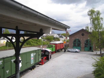 Blick auf den Bahnsteig Ein historischer Zug steht unter einem überdachten Bahnsteig, umgeben von bewölkten Himmeln und Grün.