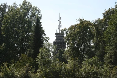 Bismarckturm Velbert Ein steinerner Turm ragt zwischen dicht belaubten Bäumen hervor, umgeben von blauem Himmel.