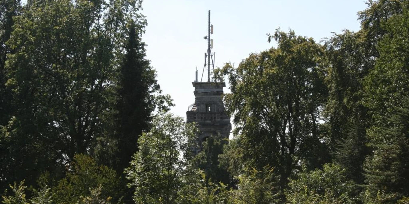 Bismarckturm Velbert Ein steinerner Turm ragt zwischen dicht belaubten Bäumen hervor, umgeben von blauem Himmel.