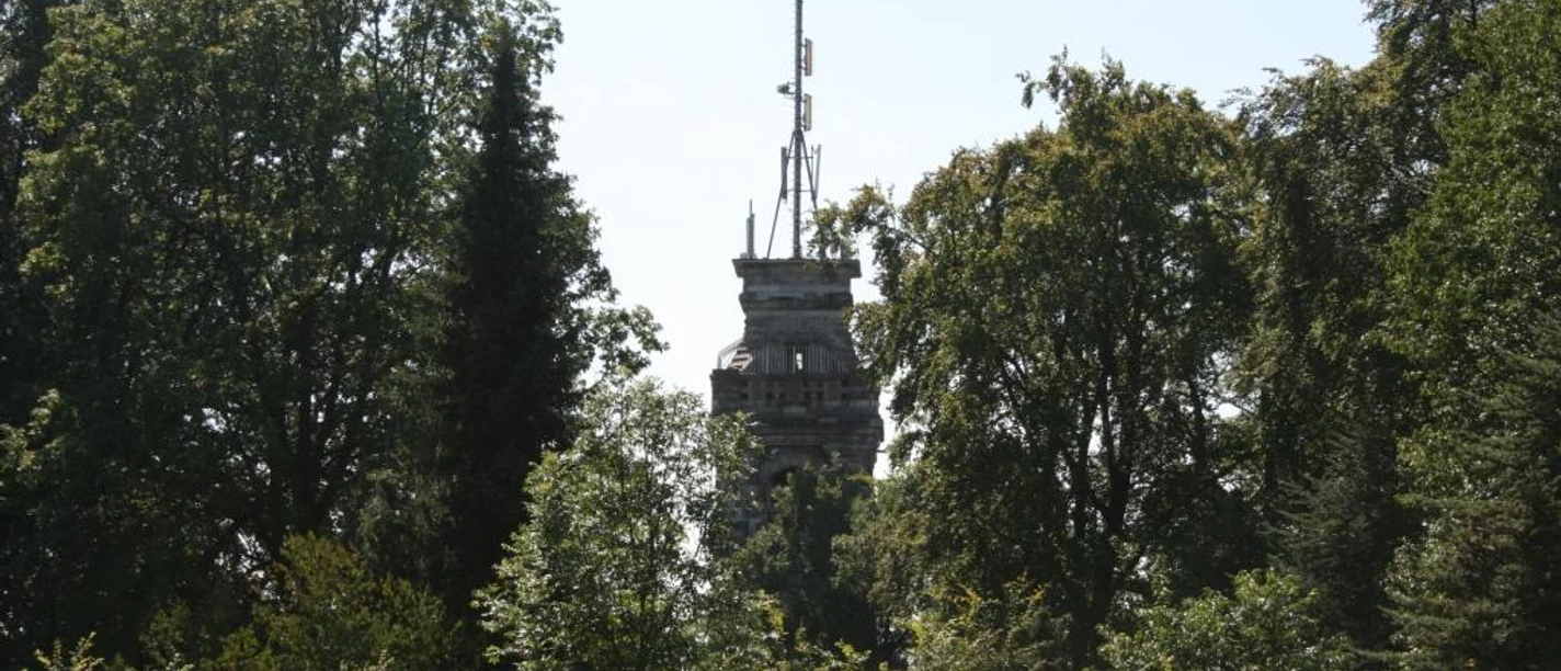 Bismarckturm Velbert Ein steinerner Turm ragt zwischen dicht belaubten Bäumen hervor, umgeben von blauem Himmel.