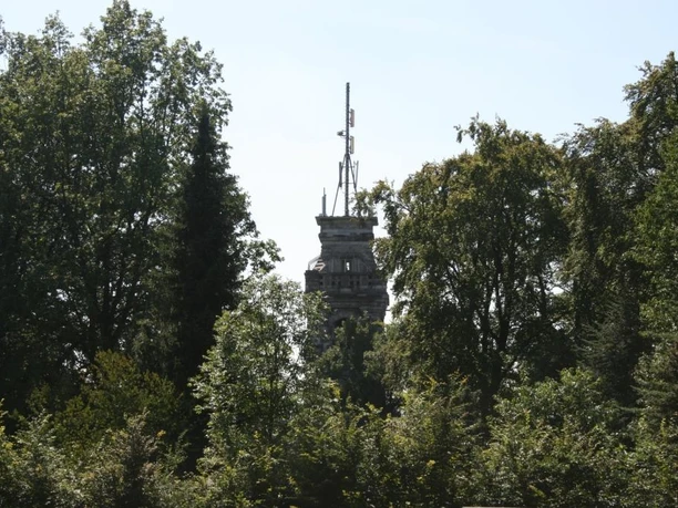 Bismarckturm Velbert Ein steinerner Turm ragt zwischen dicht belaubten Bäumen hervor, umgeben von blauem Himmel.