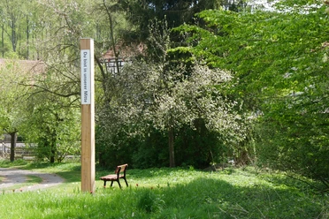 Bibel-Pfahl-Rheder Ein hölzerner Pfahl mit der Inschrift "Du bist in unserer Mitte" in einer grünen, bewaldeten Umgebung.