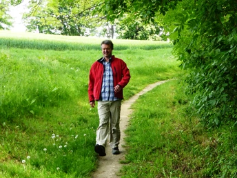 Auf schmalem Pfad hinab zum Schwarzbach Ein Wanderer in roter Jacke spaziert auf einem schmalen Pfad durch grünes Gras und dichte Bäume.