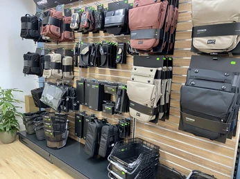 Bikefactory5.jpeg Verschiedene Fahrradtaschen sind in einem Geschäft an einer Wand präsentiert. Links steht eine Pflanze. Der Boden ist aus Holz.