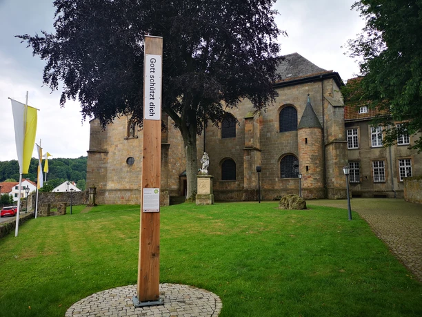 Ein hölzerner Bibel-Pfahl mit der Inschrift "Gott schützt dich" steht vor einer Kirche.