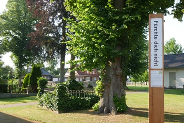 Bibel-Pfahl Peckelsheim Bibel-Pfahl mit der Aufschrift "Fürchte dich nicht", umgeben von Bäumen und einem kleinen Garten.