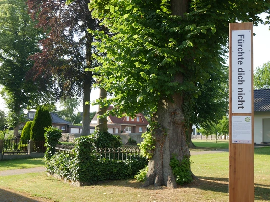 Bibel-Pfahl Peckelsheim Bibel-Pfahl mit der Aufschrift "Fürchte dich nicht", umgeben von Bäumen und einem kleinen Garten.