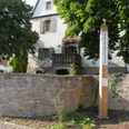 Ein Bibel-Pfahl in Bonenburg steht vor einem Haus, von Bäumen umgeben und mit einer Steinmauer.