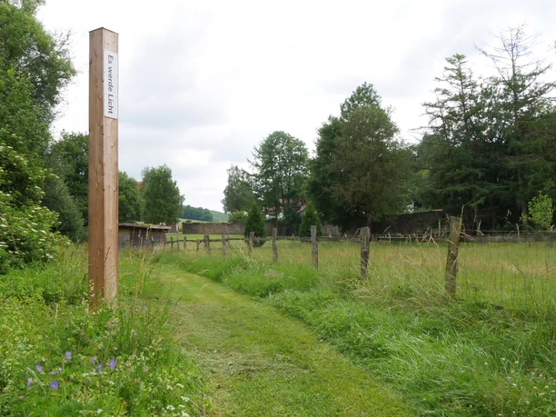 Ein hölzerner Bibel-Pfahl mit der Aufschrift "Ein wahres Licht" steht inmitten einer grünen Wiese.