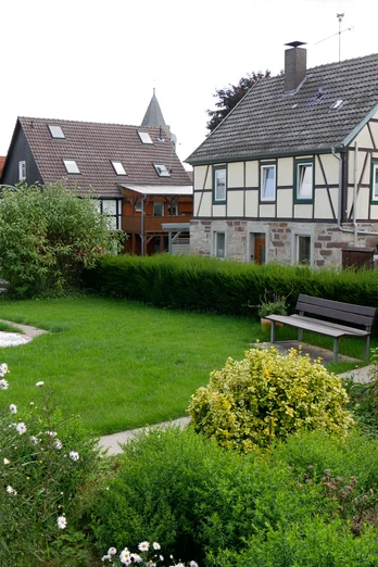 Bibel-Pfahl Germete Dorfplatz mit gepflegtem Garten, traditionellem Fachwerkhaus und Bibel-Pfahl im Vordergrund.