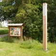 Ein hoher Holzpfahl mit der Aufschrift "Gott ist Geist" steht neben einer Infotafel am Wegesrand.
