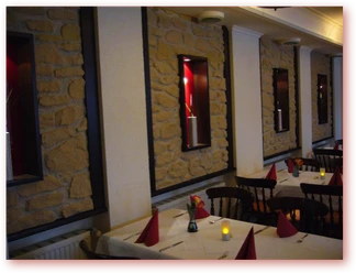 Am Kamin Restaurantinterieur mit Steinwand, gedeckten Tischen, roten Servietten und warmem Kerzenschein.